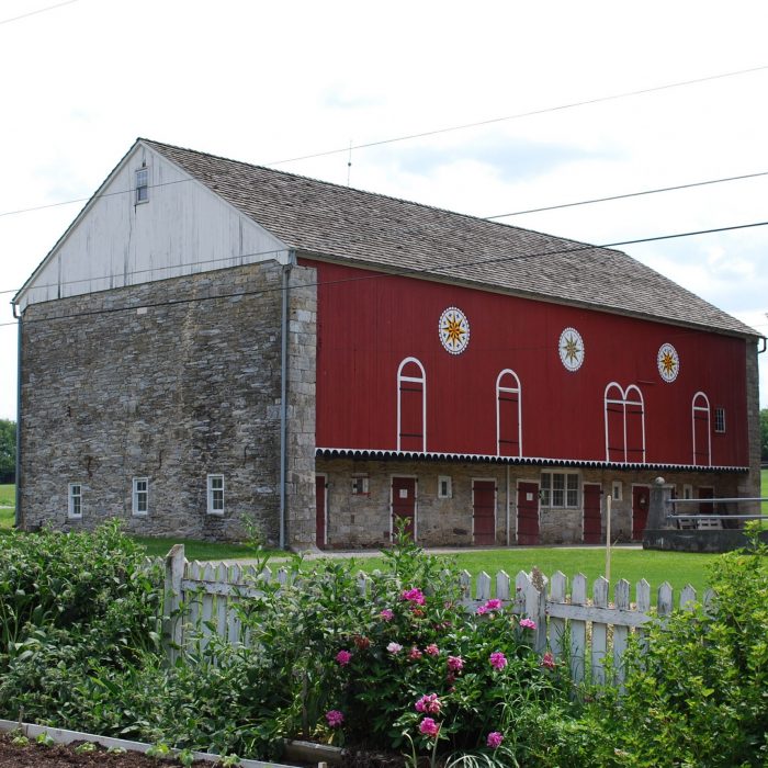 Image of the forebay side of the red and stone bank barn. The barn also has three barn stars painted along the side.