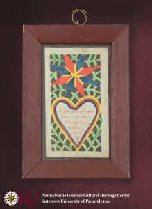 A framed cut paper Valentine featuring a star above a heart, and a lattice of green sprigs, and a sentimental German inscription of affection.